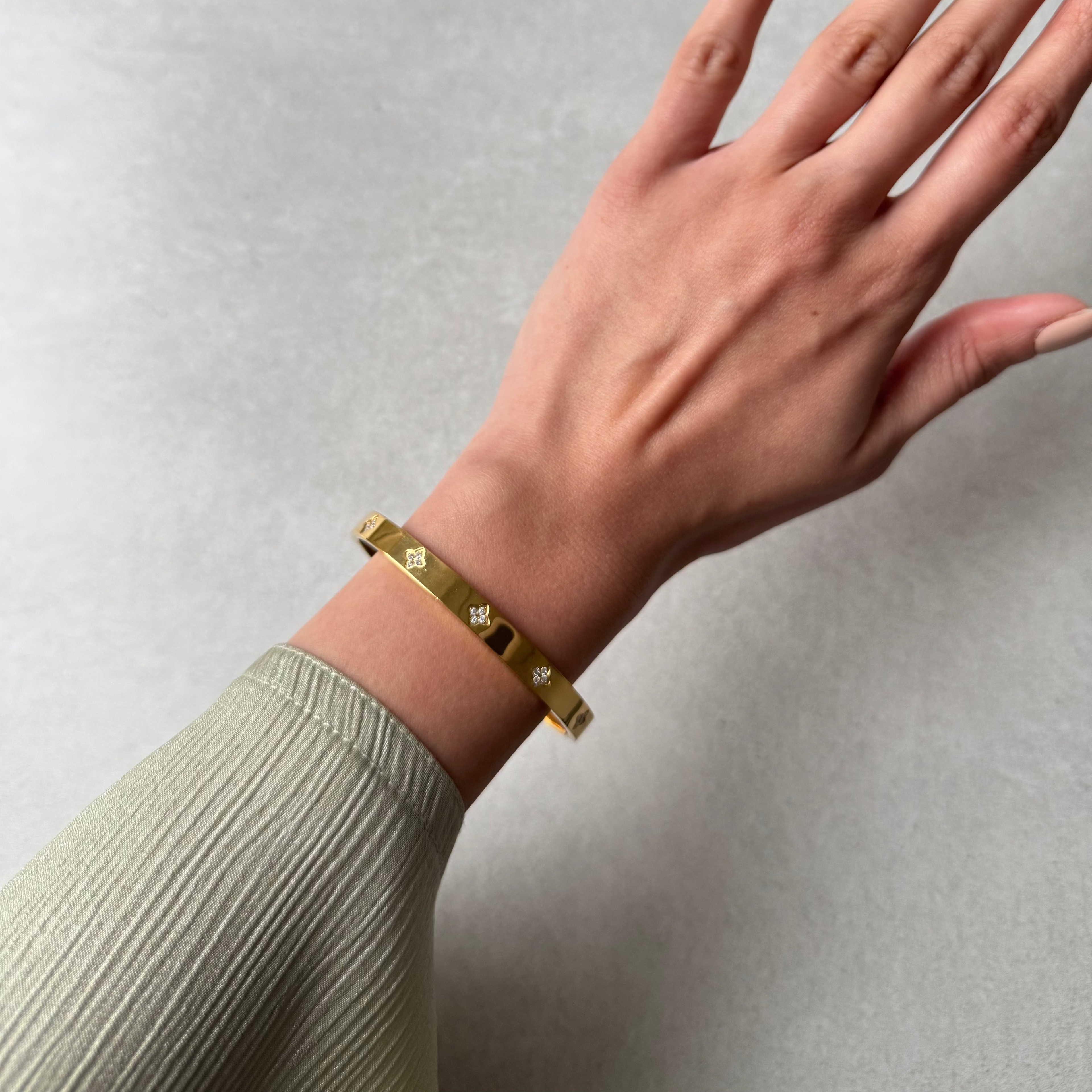 A model wearing our Sidra bangle, this is a tarnish free and waterproof bangle. The bangle is available in gold and silver. There are stones in the shape of a 4 leaf clover going around the bracelet.