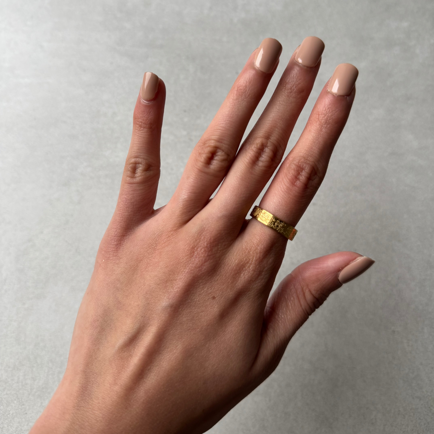 A model wearing a gold ring with an Arabic engraving of &quot;verily with hardship comes ease&quot;